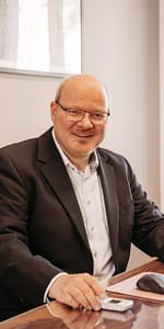 Professionelles Hochformat-Porträt von Rechtsanwalt Daniel van Heiden am Holzschreibtisch mit Computermaus in der Kanzlei van Heiden.