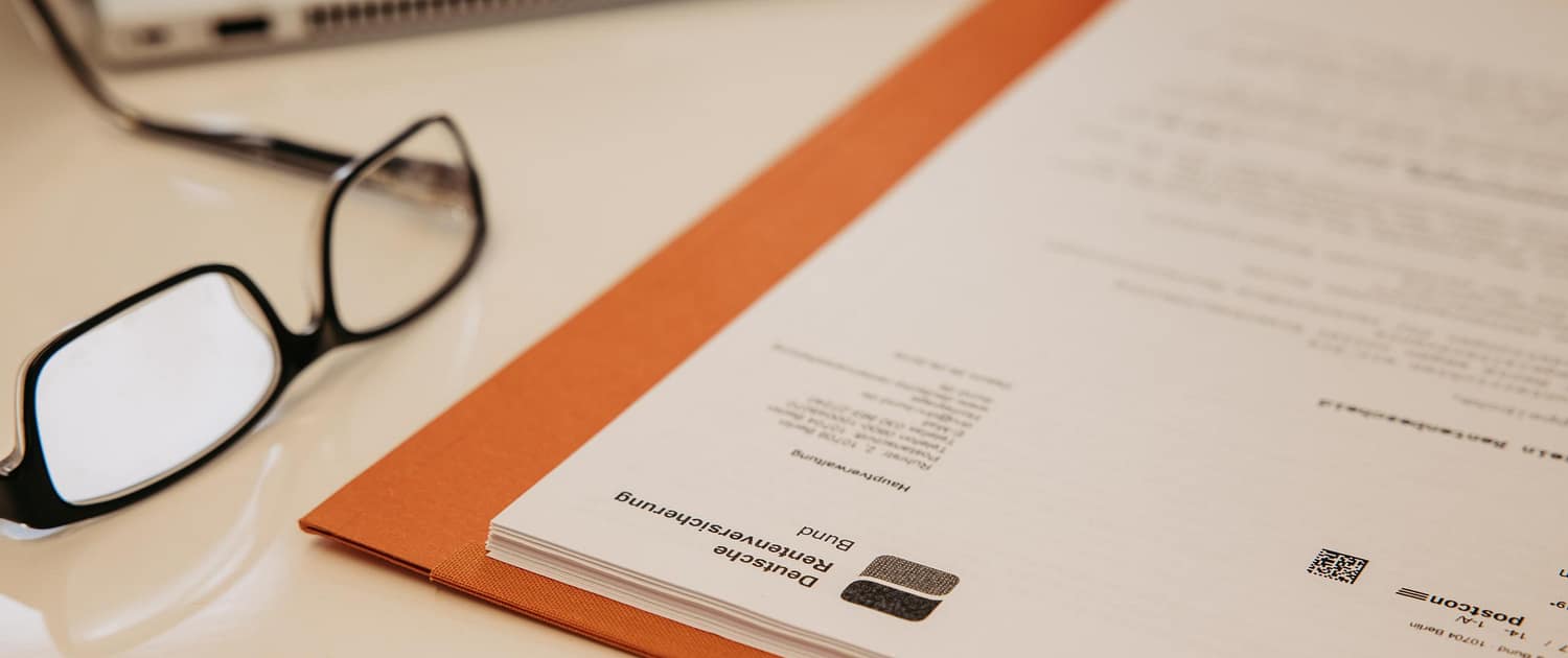 Unterlagen zur Rentenberatung – Kanzlei van Heiden Professionelle Rentenberatung: Dokumente der Deutschen Rentenversicherung Bund in einer orangen Akte auf einem Schreibtisch mit Lesebrille und Laptop.