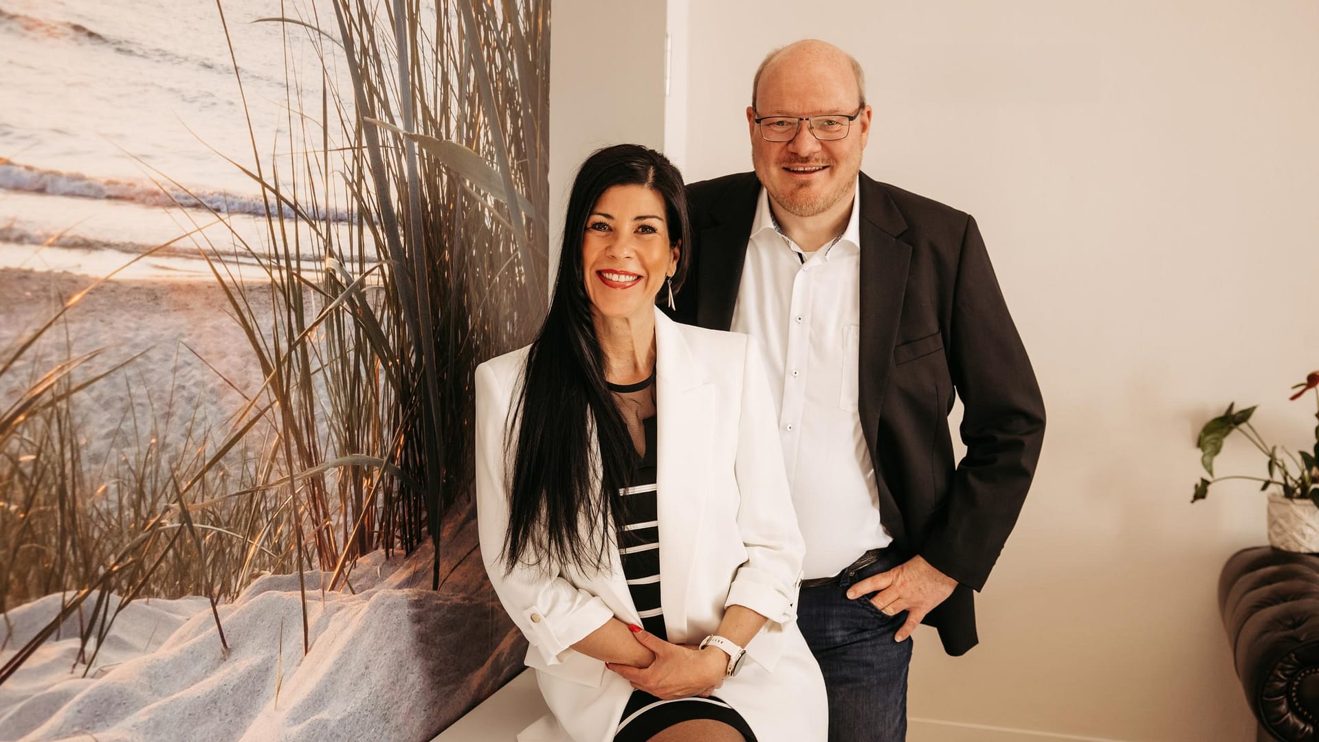 Das Team der Kanzlei van Heiden: Sandy und Daniel van Heiden Sandy van Heiden und Daniel van Heiden von der Kanzlei van Heiden vor einem maritimen Wandmotiv in ihren Kanzleiräumen.